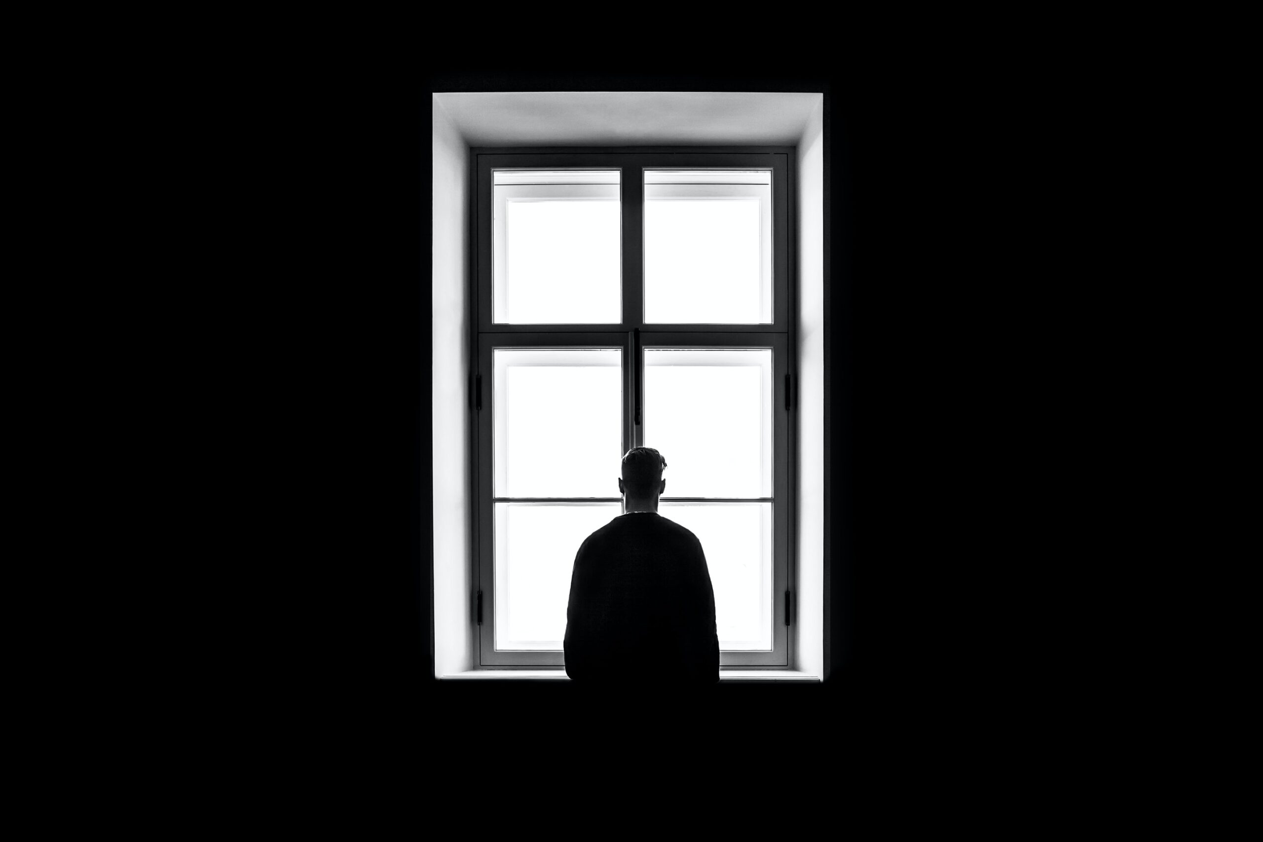 Silhouetted figure at a large window to show poor wellbeing. Photo by Sasha Freemind on Unsplash